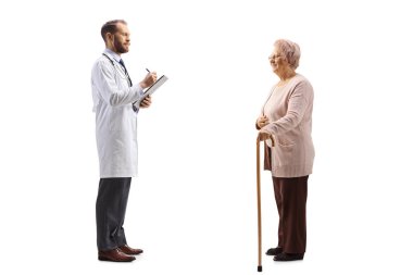 Bir doktorun doküman yazarken ve yaşlı bir kadın hastayla birlikte beyaz arka planda dikilirken tam boy profil çekimi.