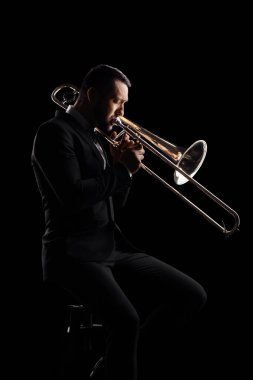 Man playing a trumpet and sitting on a chair isolated on black background