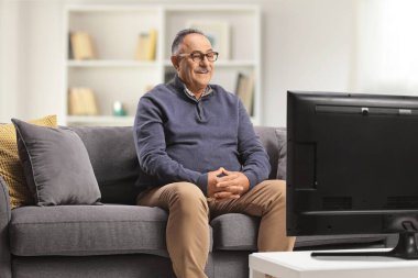 Happy mature man sitting on a sofa and watching tv at home