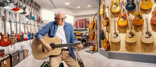 成熟した男は音楽店の中でアコースティックギターを演奏 — ストック写真