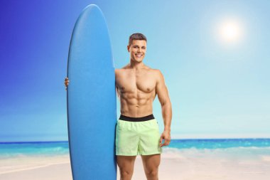 Fit young man in swimsuit standing on a beach and holding a surfing board