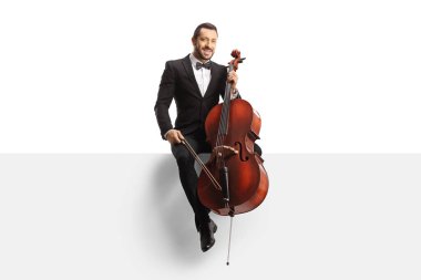Full length portrait of a musician in a black suit and bow-tie sitting on a white panel with a cello isolated on white background