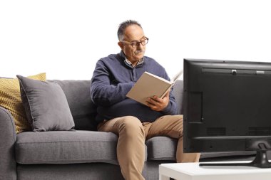Mature man sitting on a couch and reading a book in front of tv isolated on white background