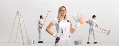 Female house painter holding a color swatch palette and male workers painting a wall 