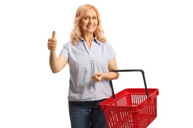 Woman with a red shopping basket smiling at camera and gesturing thumbs up isolated on white background