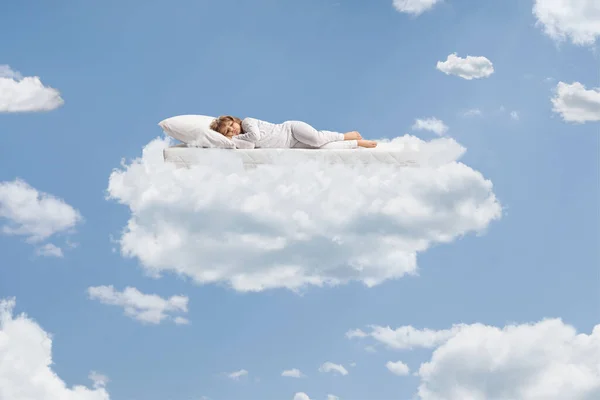 Child in pajamas sleeping over a flying mattress up in the sky on a cloud