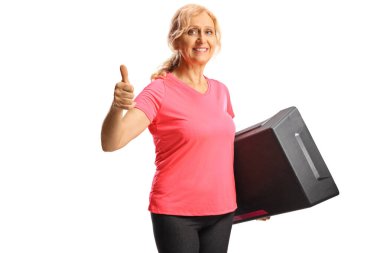 Beautiful woman holding a step aerobic platform and gesturing thumbs up isolated on white background