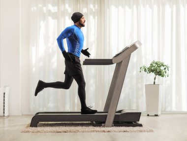 Full length profile shot of a man running on a treadmill indoors