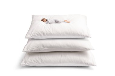 Little girl in pajamas sleeping over a pile of pillows isolated on white background