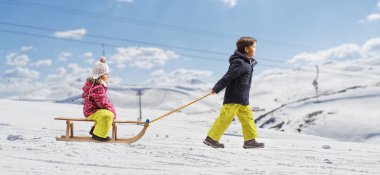 Full length profile shot of a boy pulling girl on a wooden sleigh on a snowy mountain