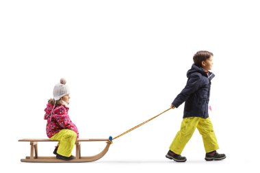 Beyaz arka planda izole edilmiş tahta kızaklı bir kızı çeken bir çocuğun tam boy profil çekimi.