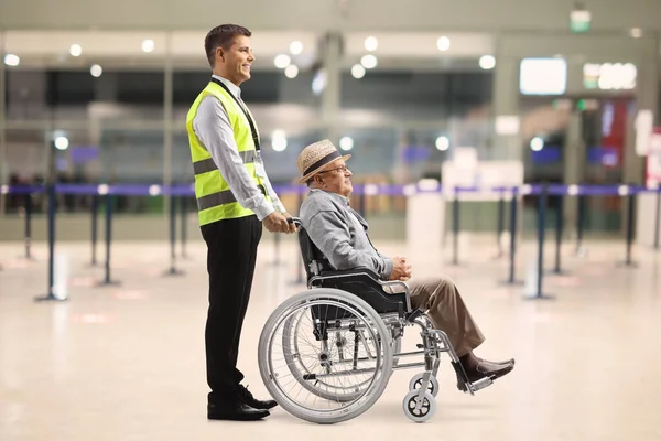Full length profile shot of a male assitance worker with a senior passenger in a wheelchair at the airport