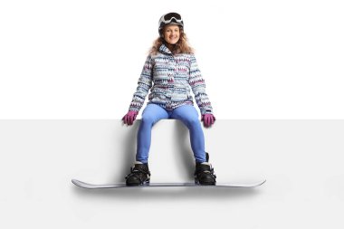 Genç bayan snowboardcu beyaz arka planda boş bir panelde oturuyor.