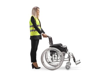 Full length profile shot of a female assitance worker standing with a wheelchair isolated on white background