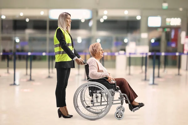 Female assitance worker at the airport standing with an older woman in a wheelchair