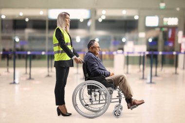 Female special assitance worker inside an airport building pushing a passanger in a wheelchair