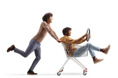 Happy young caucasian man pushing an african american guy inside a shopping cart isolated on white background