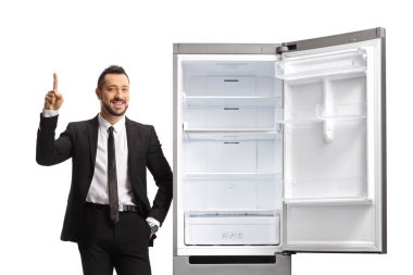 Businessman leaning on an empty fridge and pointing up isolated on white background