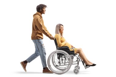 Full length profile shot of an african american man pushing a caucasian pregnant woman in a wheelchair isolated on white background