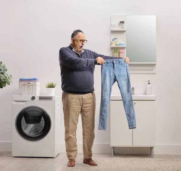 混淆不清的成熟男人从浴室里的洗衣机里拿出一条牛仔裤 — 图库照片