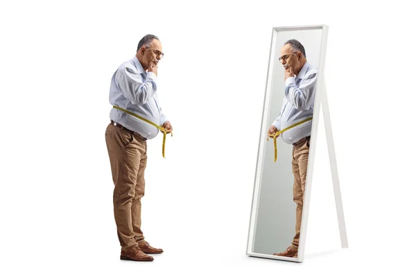 白い背景に隔離された鏡の前にテープで腰を測定している半成熟した男の完全な長さのショット — ストック写真