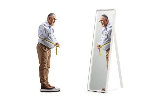 白い背景に隔離された鏡の前で腰を測定するスケール上の潜行成熟した男の完全な長さのショット — ストック写真