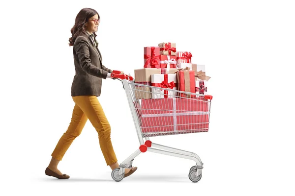 白い背景に隔離されたプレゼントでいっぱいのショッピングカートで歩く若いプロの女性のフル長さのプロフィールショット — ストック写真