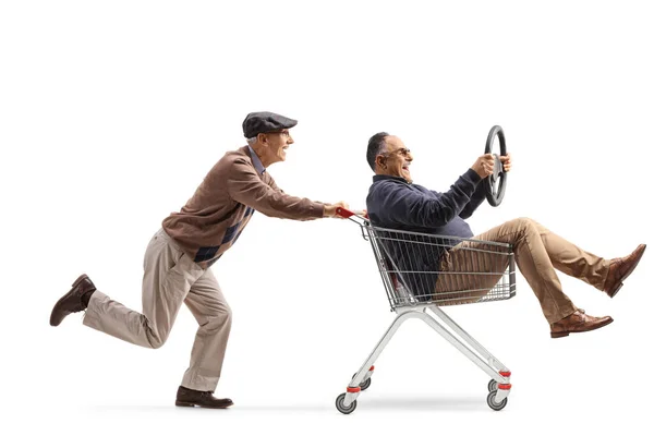 白い背景に隔離されたステアリングホイールを保持するショッピングカート内の友人を押す高齢者 — ストック写真