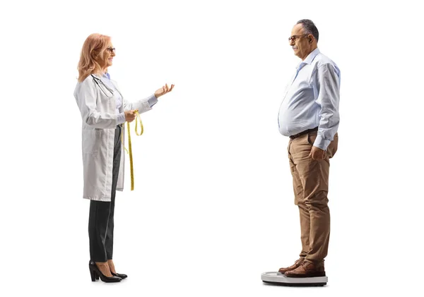白い背景に隔離された体重計に立って成熟した男と話している女性医師の完全な長さのプロフィールショット — ストック写真