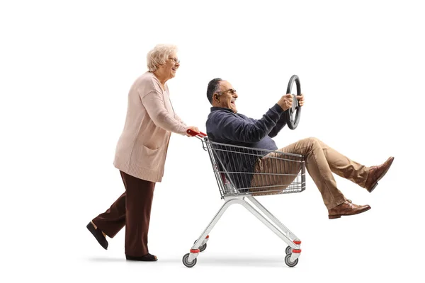 上了年纪的女人把一个成熟的男人推进购物车 手里拿着一个白色背景的方向盘 — 图库照片
