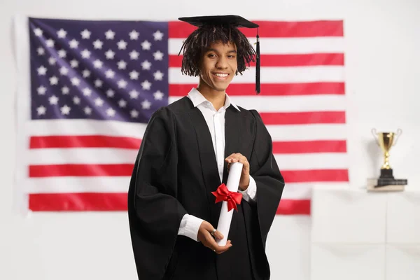 Американский Студент Мужчина Выпускном Платье Дипломом Перед Флагом Сша — стоковое фото