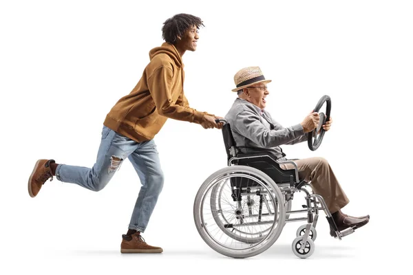 一个年轻的非洲裔美国人推着一个坐在轮椅上的成熟男人 手里拿着一个与白色背景隔离的方向盘 — 图库照片