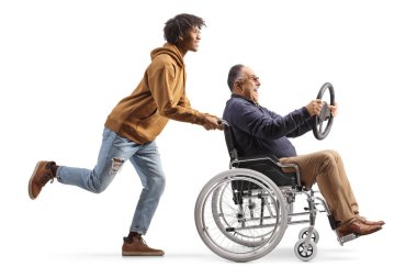 Genç Afrikalı Amerikalı bir adam tekerlekli sandalyede oturan ve elinde direksiyon tutan neşeli, olgun bir adamı itiyor. Beyaz arka planda izole edilmiş.