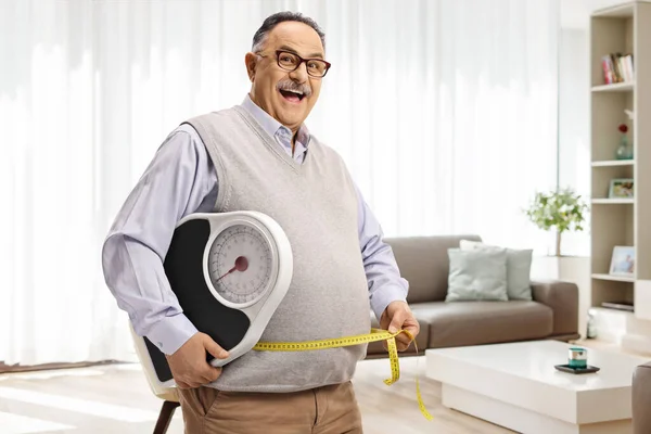 在家里客厅里 一个体重增加的成熟男人拿着度量衡和测量带 — 图库照片