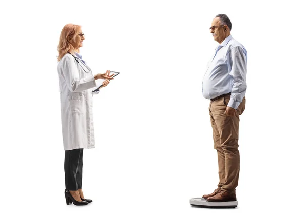 フル長さプロファイルショットの女性医師チェック重量のA成熟した男絶縁上の白い背景 — ストック写真