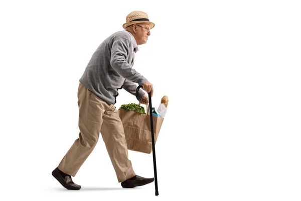 一个拿着手杖走路 提着一个白色背景的购物袋的老人的全身像照片 — 图库照片