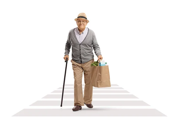一个拿着手杖走在人行横道上 提着一个白色背景的购物袋的老年男子的全长肖像 — 图库照片