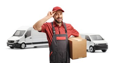 Karton bir kutu taşıyan kargo işçisi beyaz arka planda izole edilmiş kamyonetlerin önünde şapkasıyla selam veriyor.