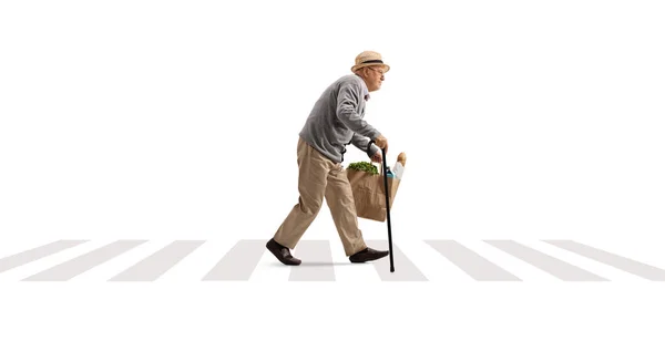 白い背景に隔離された歩行者交差点で食料品袋を持って歩く杖を持つ高齢者の完全な長さのプロフィールショット — ストック写真