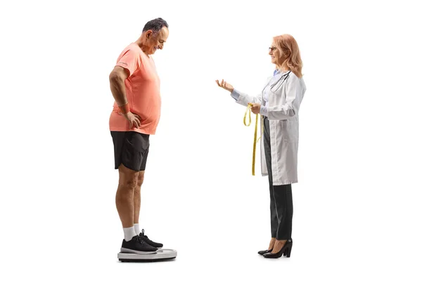 白い背景に隔離された体重計で成熟した男と話している女性医師の完全な長さのプロフィールショット — ストック写真