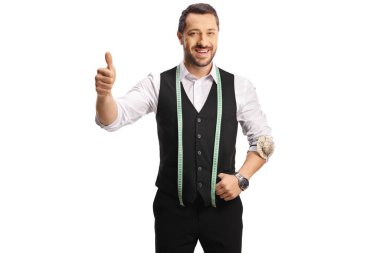 Kameraya gülümseyen ve beyaz arka planda izole edilmiş baş parmakları gösteren bir mezura taşıyan genç terzi.