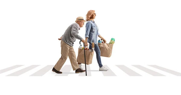 在一个白色背景隔离的人行横道上 一名妇女帮助一名老年人提着购物袋的全景照片 — 图库照片