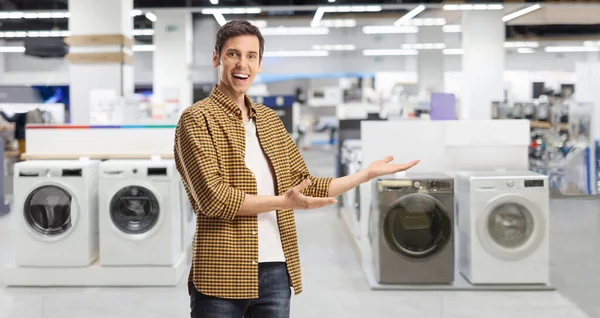 Young casual man presenting an electrical appliance shop with washing machines