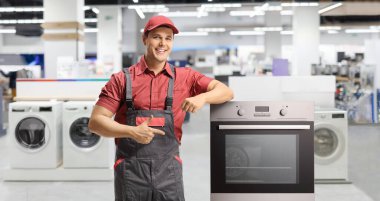 Tamirci bir dükkanın içindeki elektrikli fırını işaret ediyor.