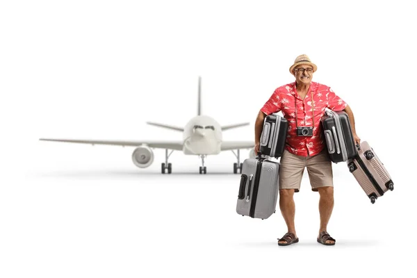 白い背景に隔離された飛行機の前で多くのスーツケースを保持している成熟した男の完全な長さの肖像画 — ストック写真