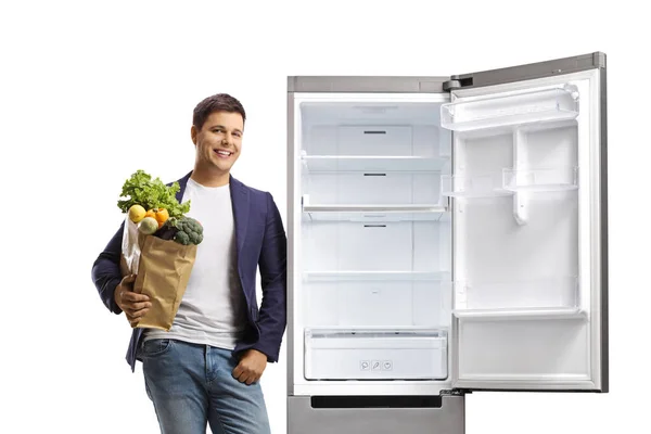 Молодой Человек Держит Пакет Продуктами Опирается Холодильник Изолированный Белом Фоне — стоковое фото
