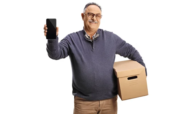 段ボール箱を持っている幸せな成熟した男と白い背景に隔離されたスマートフォンを示しています — ストック写真