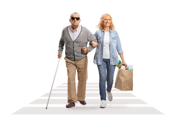 妇女帮助失明的老年人提着购物袋穿过一条被白色背景隔离的街道 — 图库照片