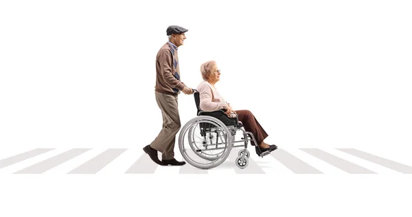 在一个白色背景隔离的人行横道上 一名老年男子推着一名坐轮椅的老年妇女 照片全长 — 图库照片