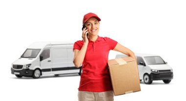 Kadın kurye elinde bir karton kutu tutuyor ve beyaz arka planda izole edilmiş bir telefon görüşmesi yapıyor. 